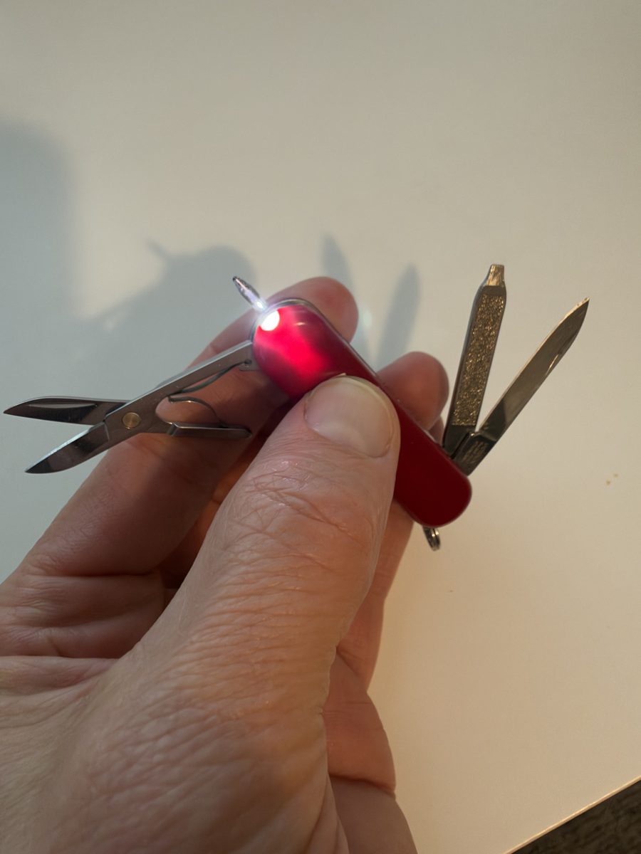 Tyler's Victorinox Swiss Army Manager, pen-and-light version, held in hand with the white light on, pen, scissors, knife and file open